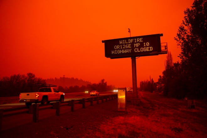 在高速公路的汽车在俄勒冈野火疏散期间的高速公路与红色天空和高闭合警报标志。
