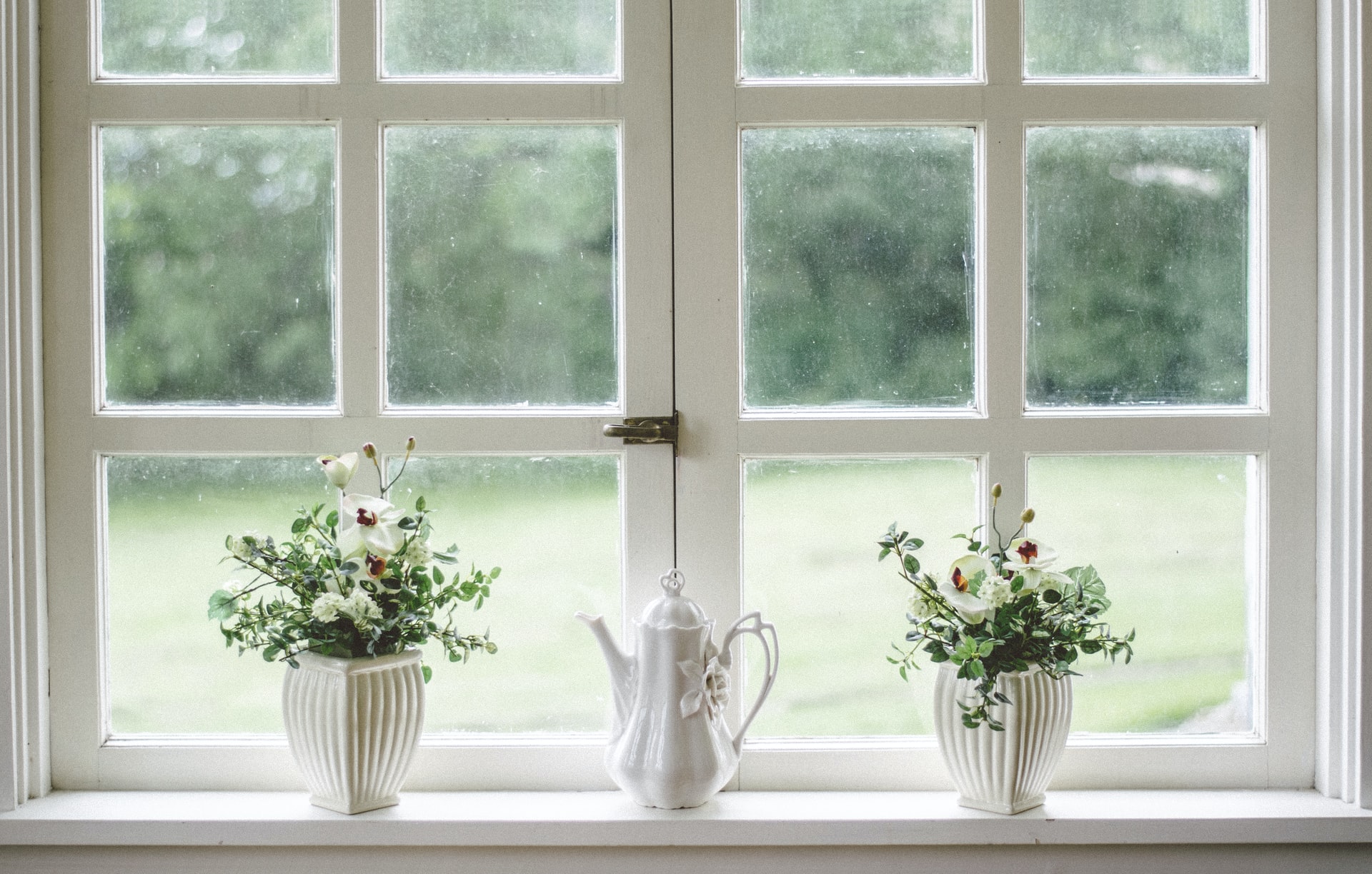 两个窗户manbetx客户端应用下载有白色涂漆的窗格，窗口的下半部分窗口锁。有两种植物坐在窗台上，在他们之间拍摄茶壶。