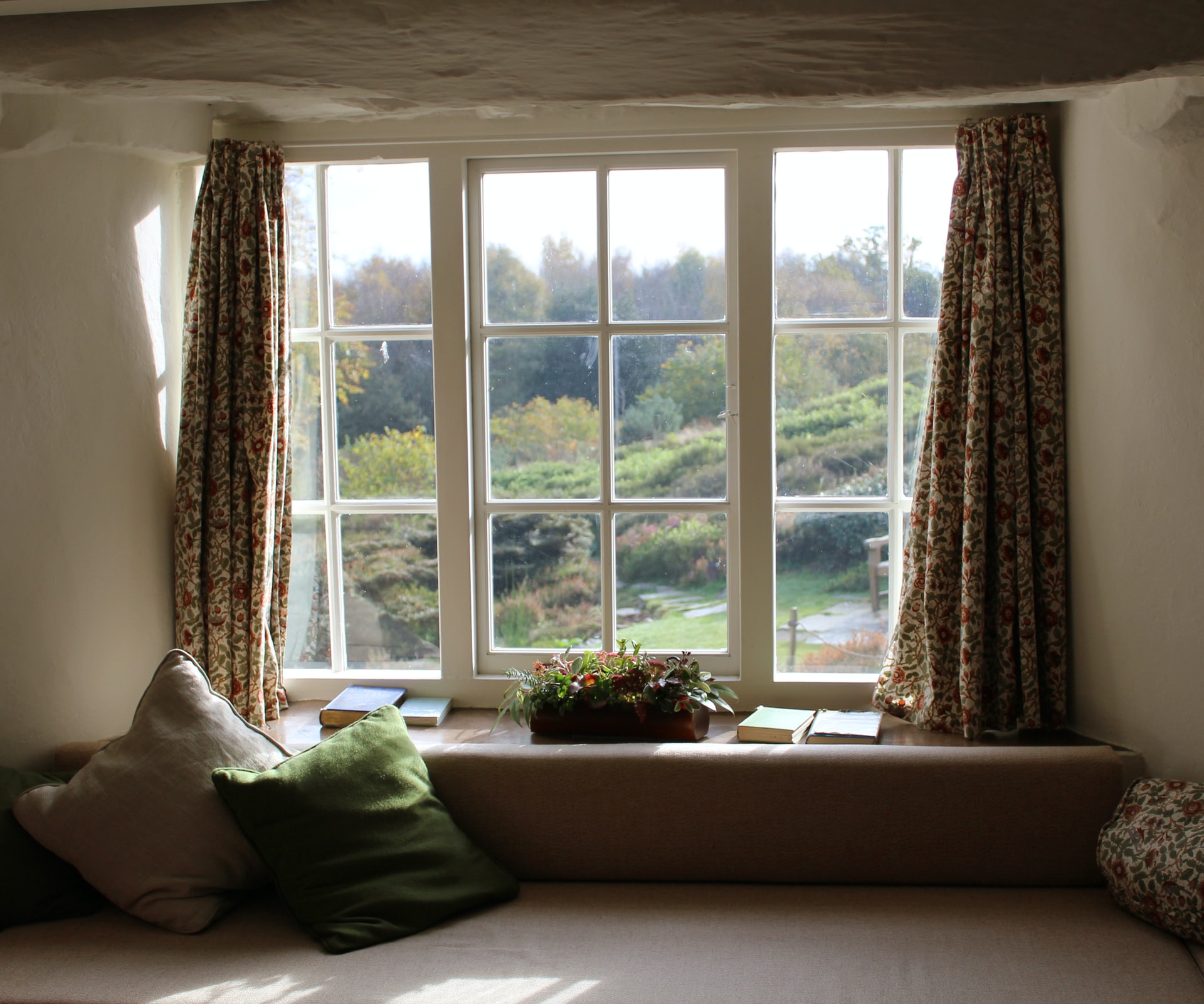 有一个旧窗口的第二层房间，看着后院。窗帘悬挂在窗户和窗台上，窗户拿着植物和一些书籍。